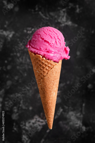 Pink ice cream in a waffle cone on a dark background