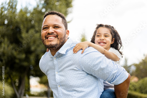 An African father plays with his daughter in an outdoor park. The adult carries the little girl happily on his back. Concept of single-parent family, separated Africans, multiethnic family.