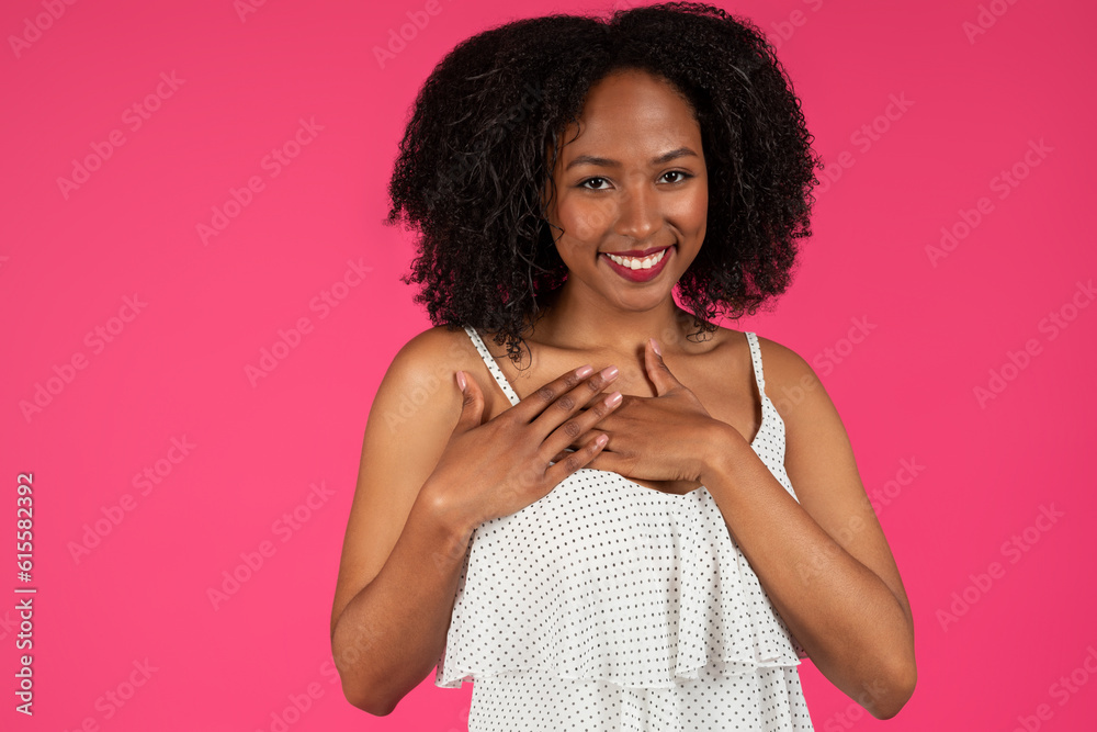 Glad young black curly lady presses hands to chest, makes sign of gratitude, thank you Glad young black curly lady presses hands to chest, makes sign of gratitude, thank you
