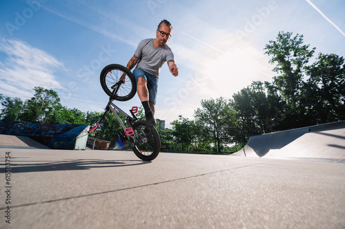 Wide-angle view of a focused middle-aged urban man practicing bmx tricks in a skate park.