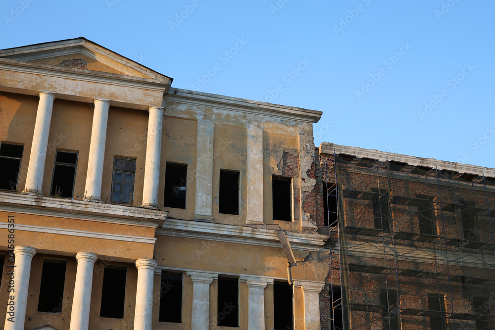 Abandoned building under renovation. An old windowless building with a yellow façade and scaffolding for workers. Exterior of an old shabby building