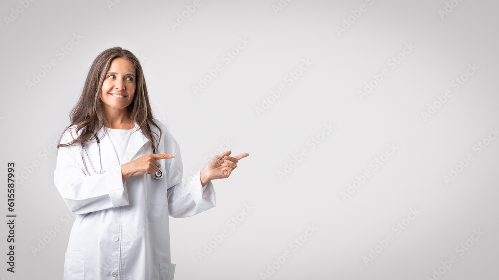 Medical insurance. Friendly caucasian senior woman in medical workwear doctor pointing aside at copy space for ad Medical insurance. Friendly caucasian senior woman in medical workwear doctor pointing aside at copy space for ad