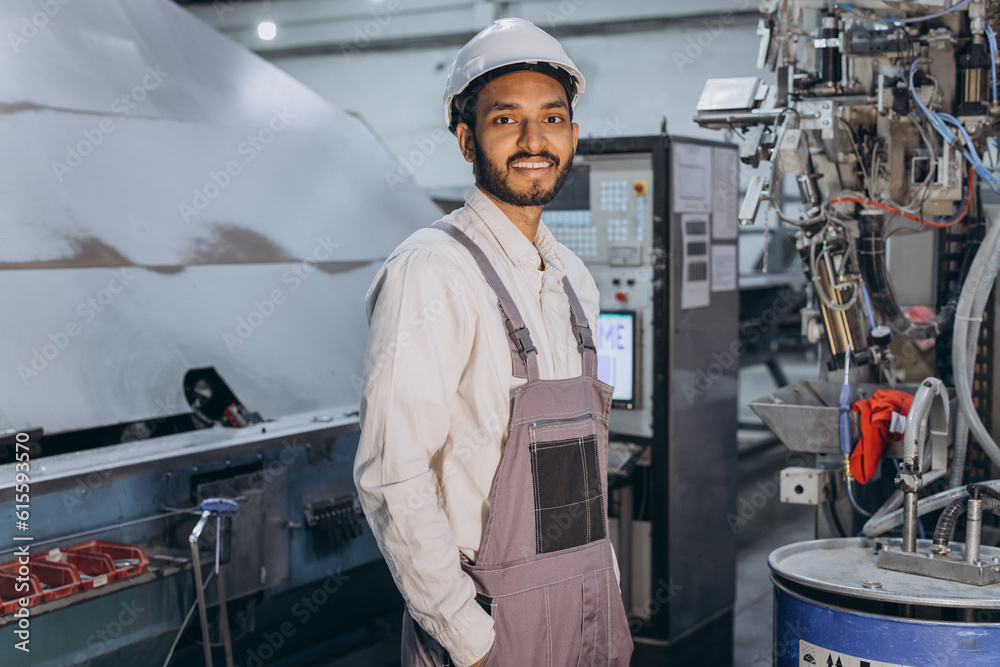 Operator of machine. Industrial worker indoors in factory. Young technician in white hard hat.