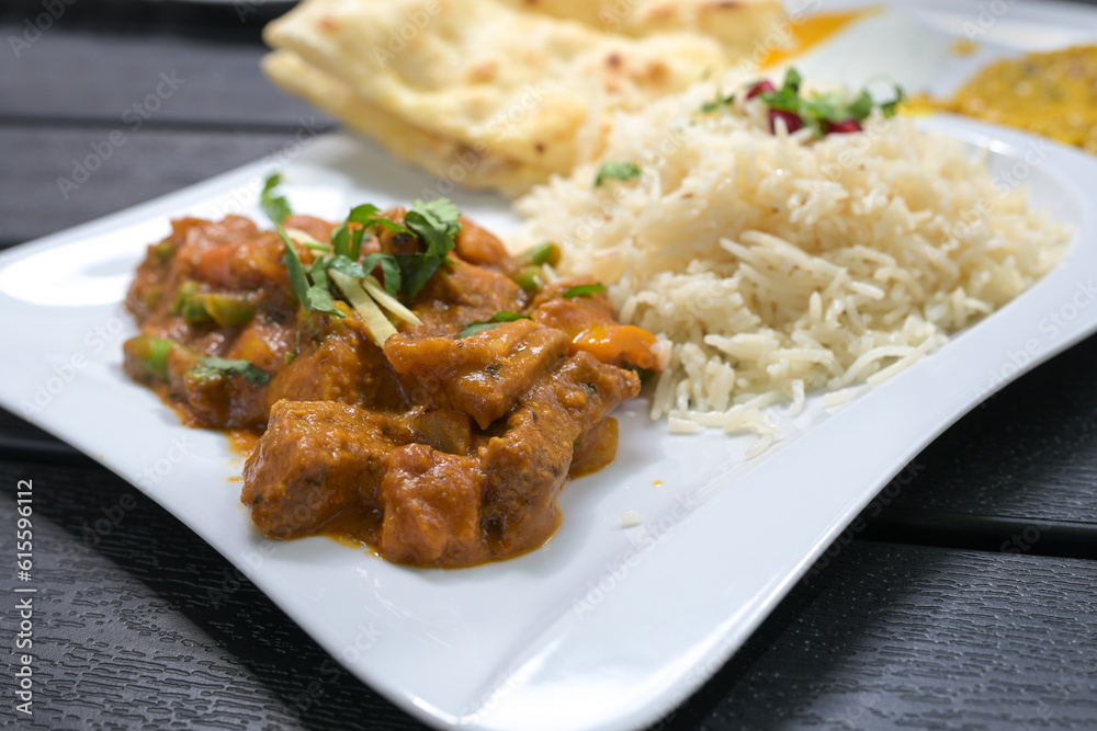 Indian meal, beef with vegetables in a spicy sauce, rice and bread on a white plate and a black table, selected focus Indian meal, beef with vegetables in a spicy sauce, rice and bread on a white plate and a black table, selected focus
