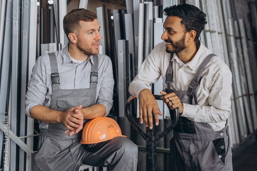 Portrait of two international workers wearing hardhats taking break from work and resting speaking to each other on a factory background with copy space