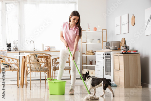 Obraz na płótnie Young woman with her French bulldog mopping floor in kitchen
