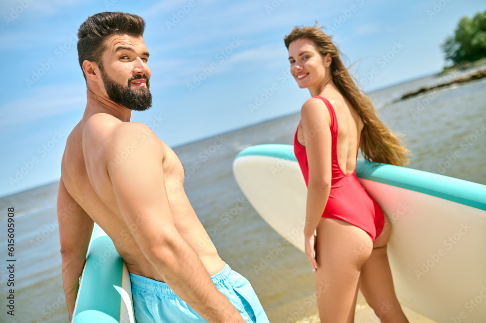 Couple with surfboards on beach, man and woman in swimsuits holding surfboards on sea coast.