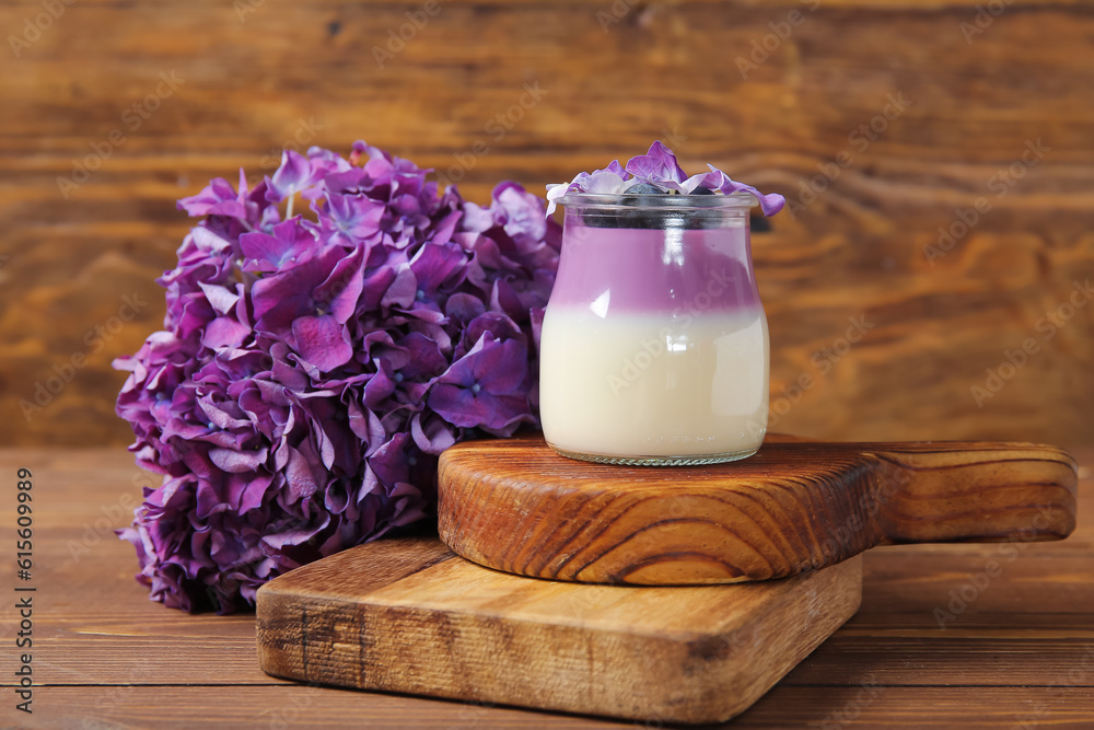Glass of panna cotta with blueberry and beautiful hydrangea flowers on wooden background