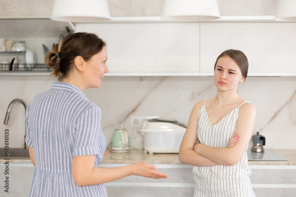 Mindful mother standing in front of kitchen cupboard with her teen daughter and explaining something to her