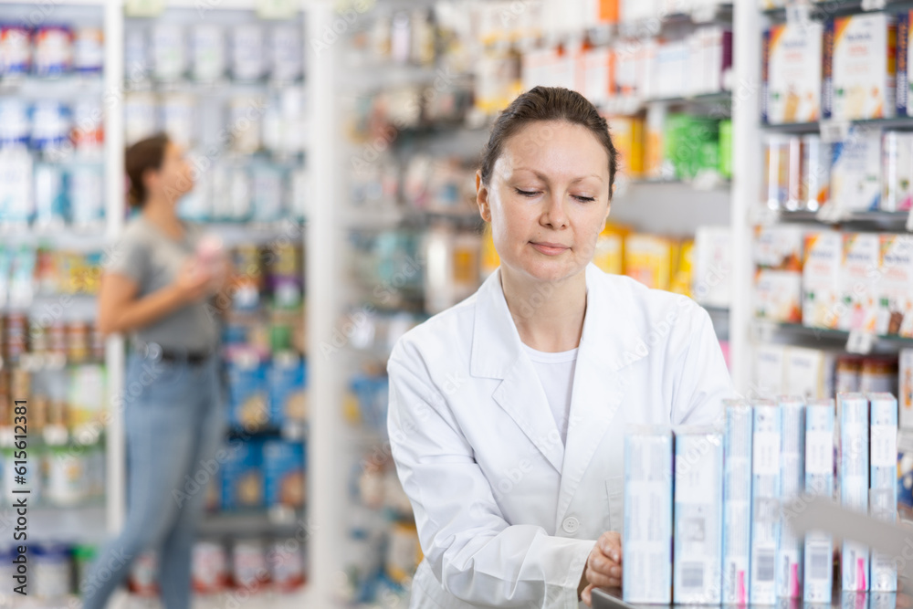 Adult woman pharmacist distributes assortment of goods on counter in pharmacy