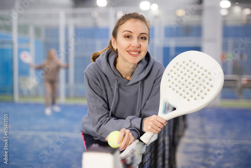 Portrait of a young active confident woman tennis player standing indoors on the court with a padel racket in her hands