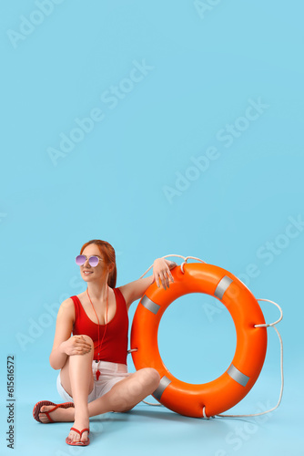 Female lifeguard with ring buoy sitting on blue background