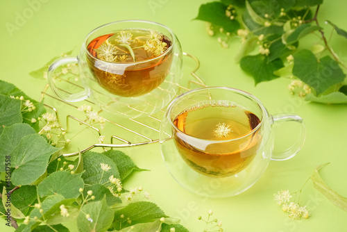 Stand with glass cups of linden tea on green background