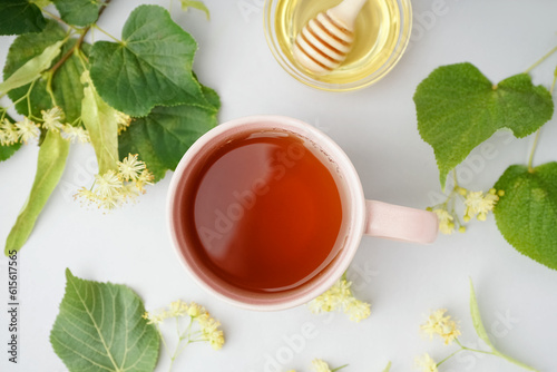Cup of linden tea and bowl with honey on grey background
