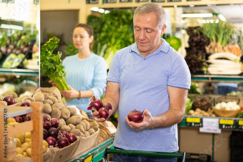 Принти на полотні in modern supermarket, man carefully selects onions and puts them in shopping ca