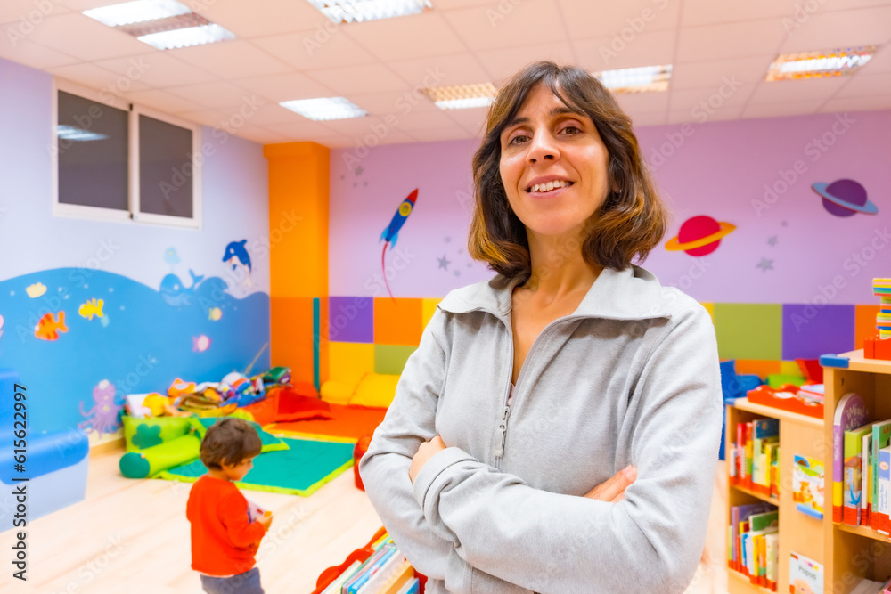 Portrait of a kindergarten or early childhood education teacher inside a kindergarten, with a child playing in the background