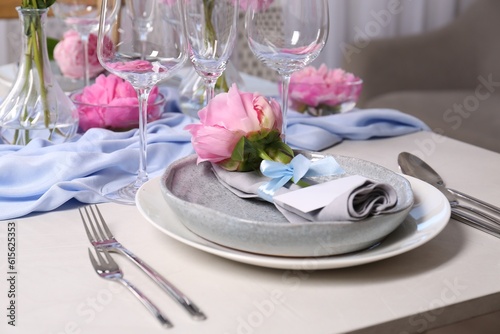 Stylish table setting with beautiful peonies, napkin and blank card indoors