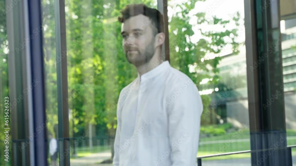 Young, handsome Caucasian adult man walking beside window in office building. Businessman looking through window. Entrepreneur, Successful manager, leader portrait walk in office center. Young, handsome Caucasian adult man walking beside window in office building. Businessman looking through window. Entrepreneur, Successful manager, leader portrait walk in office center.