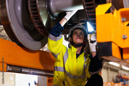 Railway technician engineer woman holds a light stick to check and fix the problem under an electric train for working at a sky train or depot maintenance plant. photo