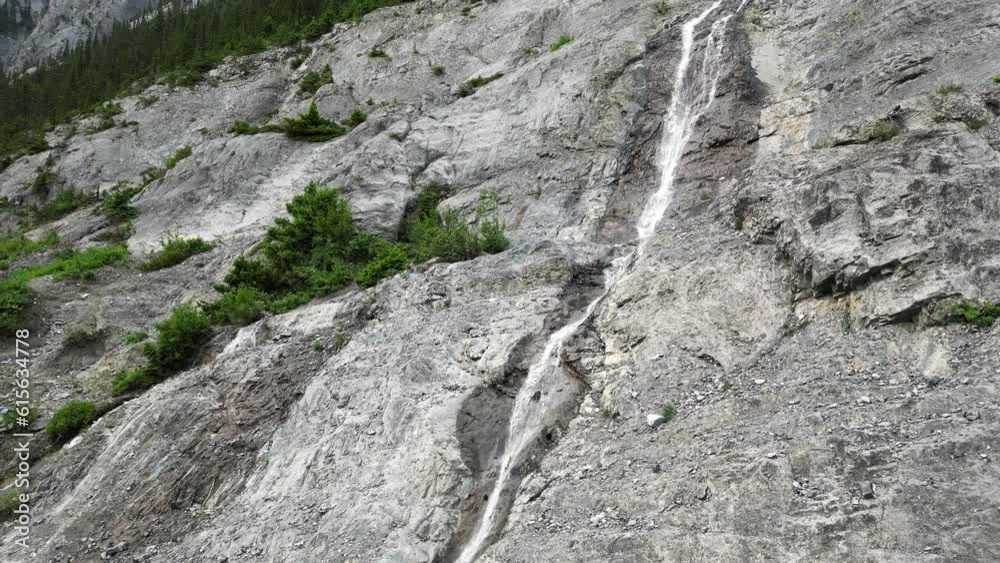 Cinematic and drone shot of water falls off a rocky mountain, melting ice in Banff national park Cinematic and drone shot of water falls off a rocky mountain, melting ice in Banff national park