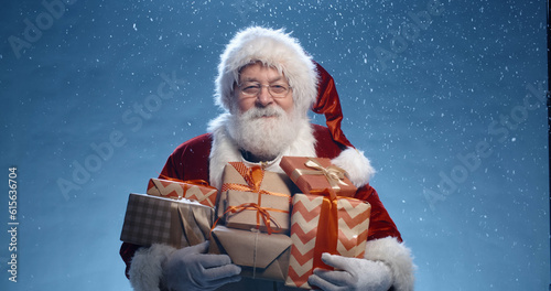 Close up shot of senior bearded man in santa clause outfit carrying gift boxes, isolated on blue background - christmas spirit, holiday mood photo