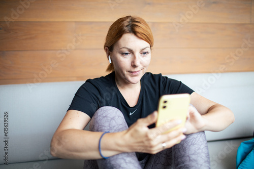 Mid adult woman using a smart phone at home while wearing her workout clothes