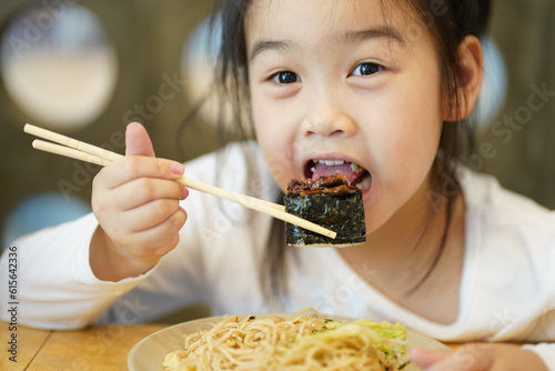 Young asian children enjoy eating Yakisoba and Sushi by using chopsticks
