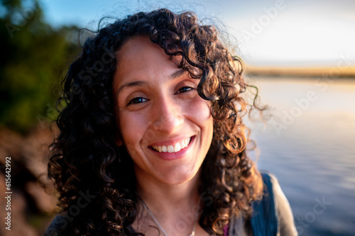 Mixed-race woman looking at camera and smiling while enjoying outdoors at sunset.