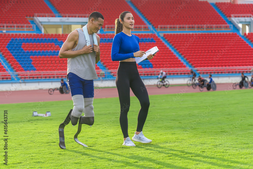 Male athlete with prosthetic blades, alongside female trainer, outlining the day's speed running training at the sports stadium