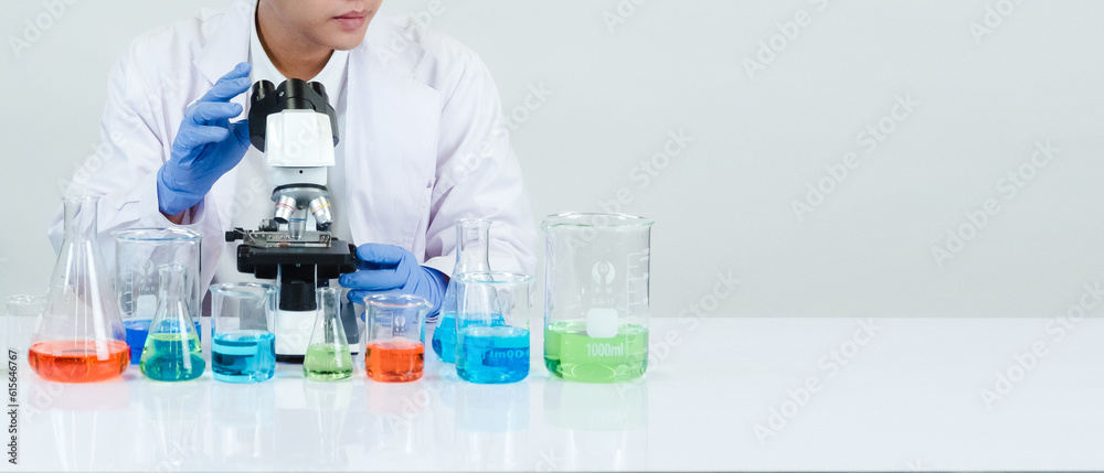 Asian male student scientist Wearing a doctor's gown in the lab looking at the chemist. caused by mixing reagents in scientific research laboratories with test tubes and microscope on the table Asian male student scientist Wearing a doctor's gown in the lab looking at the chemist. caused by mixing reagents in scientific research laboratories with test tubes and microscope on the table