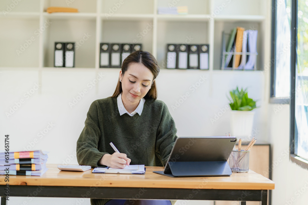 Asian businesswoman in suit sitting on desk in office, with computer document graph for bookkeeping in workplace to calculate annual profit by function, business concept