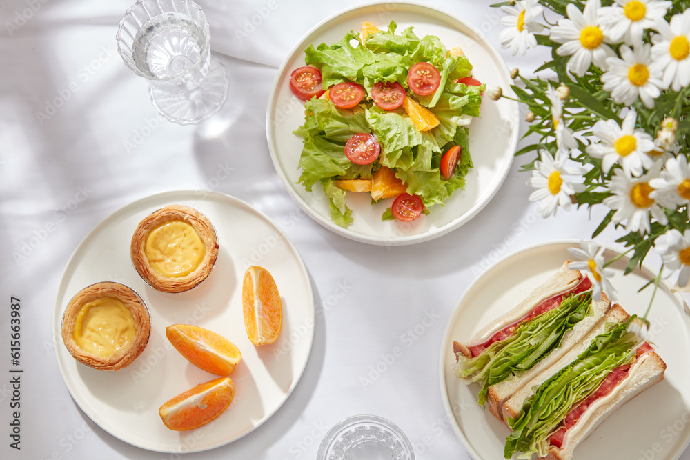 Healthy breakfast for people to lose weight, keep fit with fresh salad, sandwich, orange slice decorated on round white plates and glass of water on white background. Top view, flat lay.