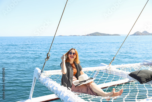 Asian woman sitting and relaxing on catamaran net enjoying seascape on summer vacation
