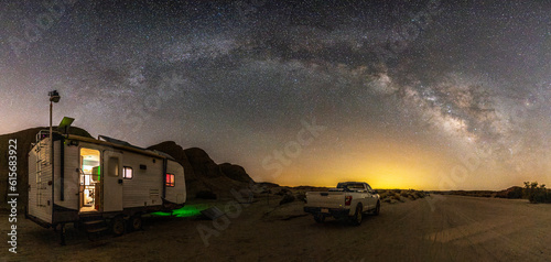 Travel trailer and pickup truck in a remote location in Anza-Borrego Desert State Park. Milky Way galaxy and stars shine in the sky above.