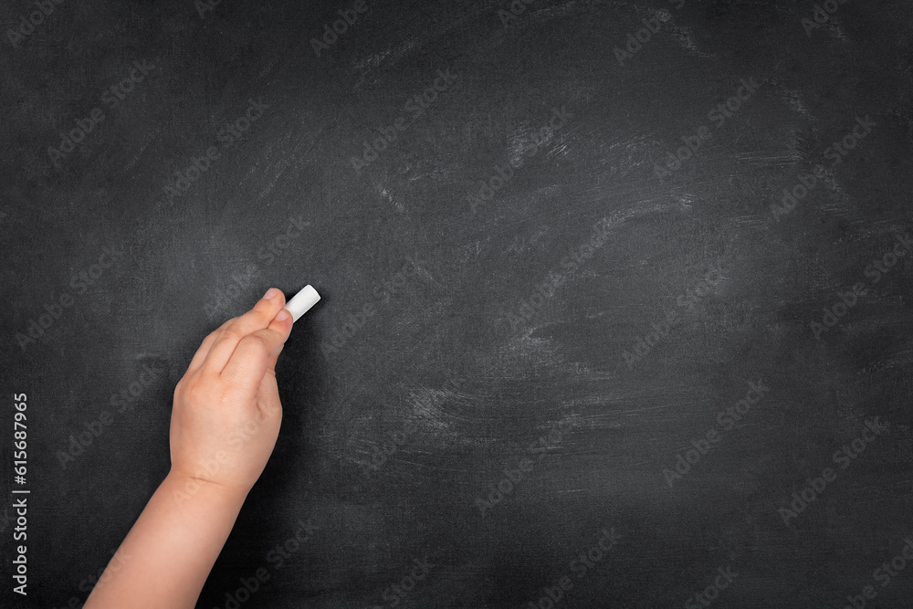 Left-handed child writing with chalk on empty school blackboard, copy space Left-handed child writing with chalk on empty school blackboard, copy space