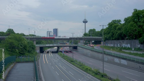 Traffic Flow and Cologne Skyline. Witness bustling cars with light strokes on a highway, a prominent TV tower, moving clouds, and Cologne's panoramic skyline in the evening. Energy and dynamism. 001 photo