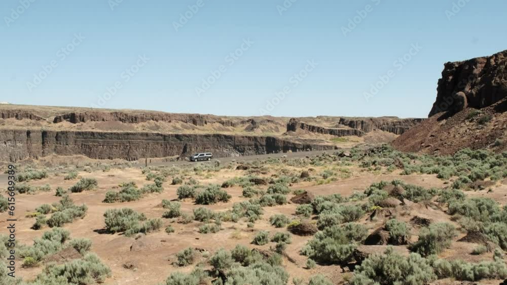 Truck drives on road past Frenchman Coulee cliffs against blue sky Truck drives on road past Frenchman Coulee cliffs against blue sky