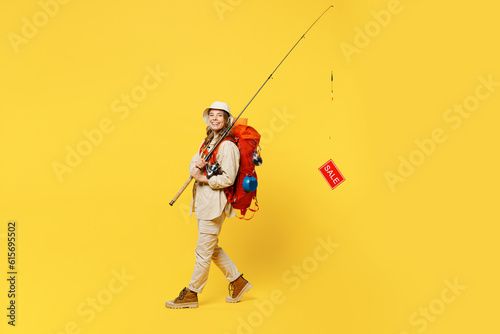 Full body young woman carry bag stuff mat hold fishing rod with sale text isolated on plain yellow background. Tourist leads active lifestyle walk on spare time. Hiking trek rest travel trip concept.