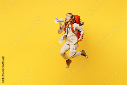 Full body side profile view young woman carrying bag with stuff mat jump high scream in megaphone isolated on plain yellow background. Tourist walk on spare time. Hiking trek rest travel trip concept.