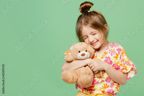 Little happy child kid girl 6-7 year old in casual clothes have fun hold hug teddy bear plush toy isolated on plain pastel green background studio portrait Mother's Day love family lifestyle concept