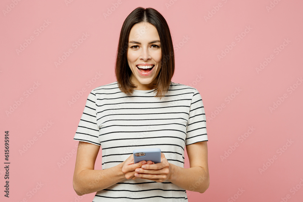 Young surprised shocked caucasian woman wear casual clothes t-shirt hold in hand use mobile cell phone look camera isolated on plain pastel light pink background studio portrait. Lifestyle concept. Young surprised shocked caucasian woman wear casual clothes t-shirt hold in hand use mobile cell phone look camera isolated on plain pastel light pink background studio portrait. Lifestyle concept.