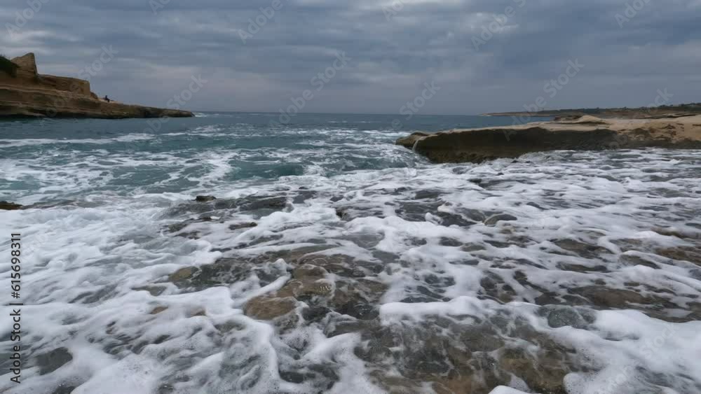 Cinematic shot of a deep blue ocean swell violently splashing over the rocky coast on a cloudy day. Cinematic shot of a deep blue ocean swell violently splashing over the rocky coast on a cloudy day.