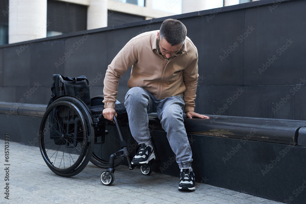 Young man with disability trying to sit in wheelchair while spending time outddoors