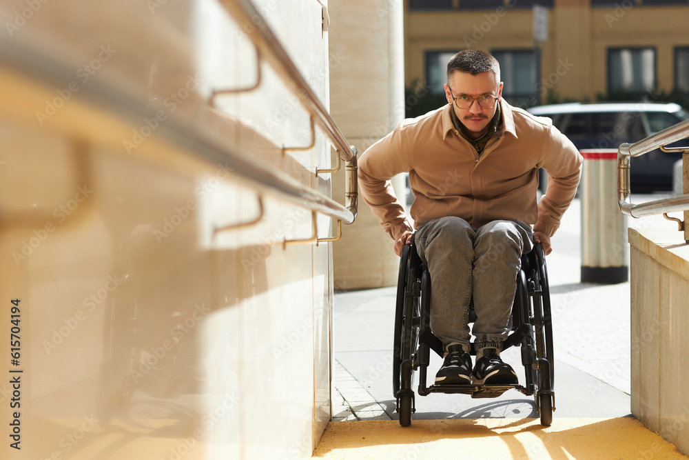 Young man in wheelchair moving up the ramp of building