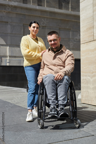 Vertical image of young man with disability looking at camera while walking with his friend in the city