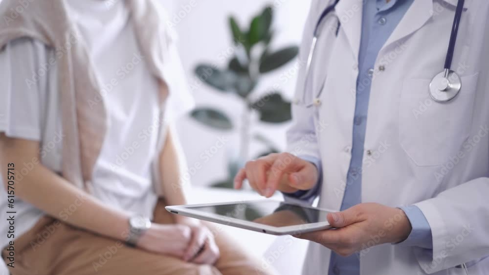 Doctor is using tablet computer while patient is sitting near. Unknown senior physician is at work. Medicine and health care concept Doctor is using tablet computer while patient is sitting near. Unknown senior physician is at work. Medicine and health care concept