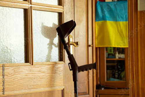 An elbow crutch stands near the door in the apartment and on the background of the flag of Ukraine, rehabilitation after an injury in the war in Ukraine at home