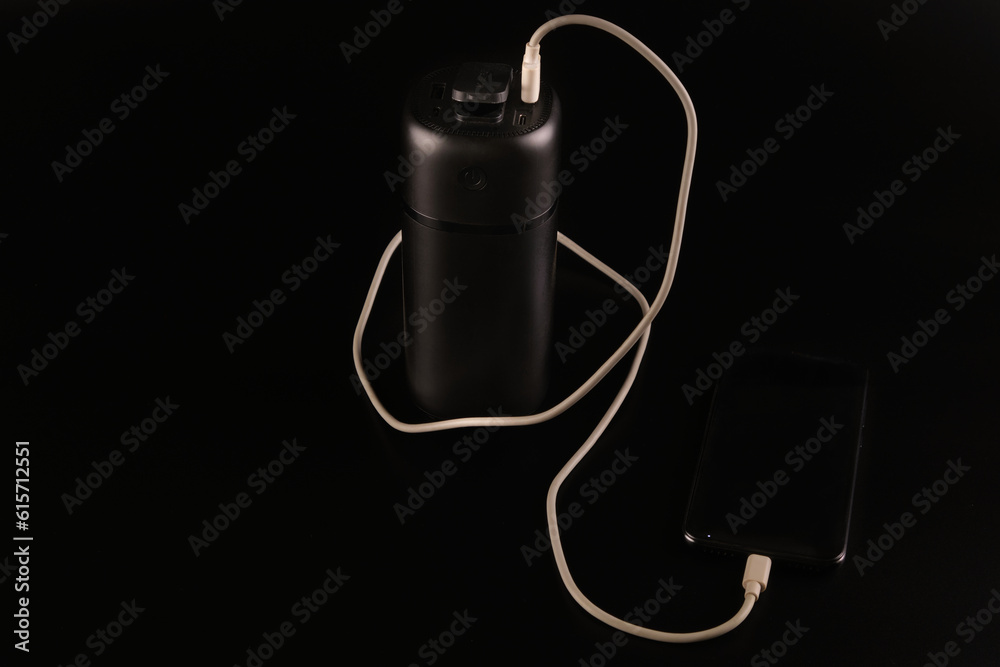 Obraz premium powerbank black on a black background, usb cable, smartphone, plug, light and reflection