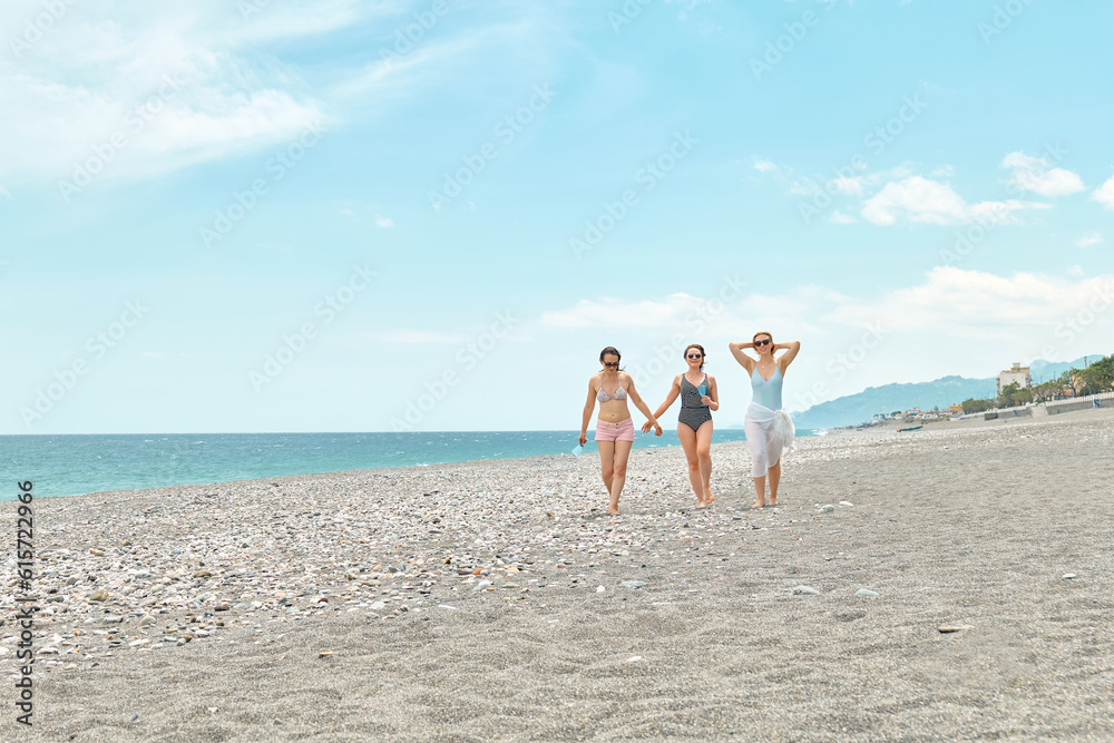 Three women friends walking on the beach and laughing on a summer day. Cheerful females enjoying together summer vacation near the sea. Three women friends walking on the beach and laughing on a summer day. Cheerful females enjoying together summer vacation near the sea.