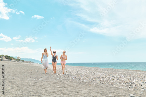 Three women friends walking on the beach and laughing on a summer day. Cheerful females enjoying together summer vacation near the sea.